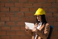 Young beautiful woman in brown coat, yellow workman`s helmet and blueprint tube, working with her tablet. Business concept, Royalty Free Stock Photo