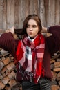 Young beautiful woman with brown hair in a knitted burgundy sweater with a checkered trendy scarf stands near an old shed outdoors Royalty Free Stock Photo