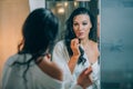 Young beautiful woman brunette in the bathroom, and white bathrobe making make-up near mirror.