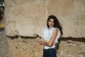 Young and beautiful woman, brunette, with curly hair, wearing a white shirt and jeans, with her arms crossed, leaning against a Royalty Free Stock Photo