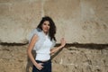 Young and beautiful woman, brunette, with curly hair, wearing a white shirt and jeans, leaning against a stone wall. Concept Royalty Free Stock Photo