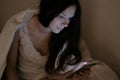 Young beautiful woman brunette looks at social networks in her mobile phone in bed before sleeping and smiles. Royalty Free Stock Photo