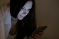 Young beautiful woman brunette reads a book in her mobile phone in bed before sleeping and smiles. Royalty Free Stock Photo