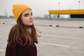 Young beautiful woman in burgundy coat and yellow hat walks along the roof of the parking lot. Loneliness, mindfulness.