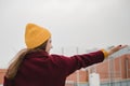 Young beautiful woman in burgundy coat and yellow hat walks along the roof of the parking lot. Loneliness, mindfulness.