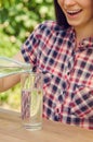 Young beautiful woman in casual shirt pours water into a glass. Royalty Free Stock Photo