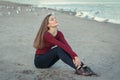 Young beautiful woman with closed eyes, long hair, in black jeans and red shirt, sitting on sand on beach among seagulls birds Royalty Free Stock Photo