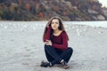 Young beautiful woman with closed eyes, long hair, wearing black jeans and red shirt, sitting on sand on beach among seagulls Royalty Free Stock Photo