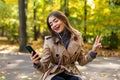 Young beautiful woman in a coat writes a message in the phone while sitting on a bench in the autumn park Royalty Free Stock Photo