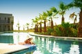 Young beautiful woman with cocktail glass, hat, bikini in blue water swimming pool at sunset party Royalty Free Stock Photo