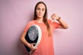 Young beautiful woman controlling weight holding weighting machine over pink background with angry face, negative sign showing Royalty Free Stock Photo