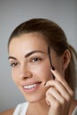 Young beautiful woman correcting shape of eyebrows on grey background, closeup.  Beauty concept. Royalty Free Stock Photo