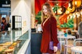 Young beautiful woman with cup of coffee in her hands is standing at window, choosing a cake Royalty Free Stock Photo