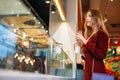 Young beautiful woman with cup of coffee in her hands is standing at window, choosing a cake Royalty Free Stock Photo