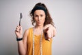 Young beautiful woman with curly hair doing diet holding fork and tape measure pointing with finger to the camera and to you, hand Royalty Free Stock Photo