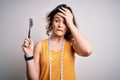 Young beautiful woman with curly hair doing diet holding fork and tape measure stressed with hand on head, shocked with shame and Royalty Free Stock Photo
