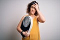 Young beautiful woman with curly hair holding weighing machine and tape measure stressed with hand on head, shocked with shame and Royalty Free Stock Photo