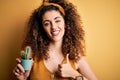 Young beautiful woman with curly hair and piercing holding pot with cactus plant happy with big smile doing ok sign, thumb up with Royalty Free Stock Photo