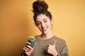 Young beautiful woman with curly hair and piercing holding pot with cactus plant happy with big smile doing ok sign, thumb up with Royalty Free Stock Photo