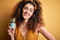 Young beautiful woman with curly hair and piercing holding pot with cactus plant with a happy face standing and smiling with a Royalty Free Stock Photo