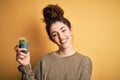 Young beautiful woman with curly hair and piercing holding pot with cactus plant with a happy face standing and smiling with a Royalty Free Stock Photo