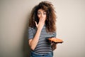 Young beautiful woman with curly hair and piercing holding tray with fresh sushi cover mouth with hand shocked with shame for Royalty Free Stock Photo