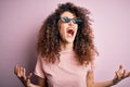 Young beautiful woman with curly hair and piercing wearing funny thug life sunglasses crazy and mad shouting and yelling with