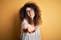 Young beautiful woman with curly hair and piercing wearing striped shirt and glasses smiling cheerful offering palm hand giving Royalty Free Stock Photo