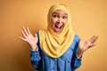 Young beautiful woman with curly hair wearing arab traditional hijab over yellow background celebrating crazy and amazed for