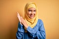 Young beautiful woman with curly hair wearing arab traditional hijab over yellow background clapping and applauding happy and
