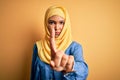 Young beautiful woman with curly hair wearing arab traditional hijab over yellow background Pointing with finger up and angry