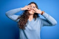 Young beautiful woman with curly hair wearing blue casual sweater over  background covering eyes with hands smiling Royalty Free Stock Photo