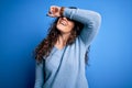 Young beautiful woman with curly hair wearing blue casual sweater over isolated background covering eyes with arm smiling cheerful Royalty Free Stock Photo