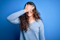 Young beautiful woman with curly hair wearing blue casual sweater over isolated background smiling and laughing with hand on face Royalty Free Stock Photo