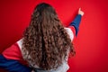 Young beautiful woman with curly hair wearing casual sweatshirt over isolated red background Posing backwards pointing ahead with Royalty Free Stock Photo