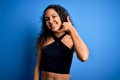 Young beautiful woman with curly hair wearing casual t-shirt standing over blue background smiling doing phone gesture with hand Royalty Free Stock Photo