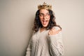 Young beautiful woman with curly hair wearing golden queen crown over white background smiling with happy face looking and Royalty Free Stock Photo