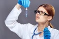 Young beautiful woman on a dark gray background holds a syringe with glasses, doctor, medicine, medical gown Royalty Free Stock Photo