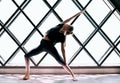 Young beautiful woman doing yoga asana reverse warrior pose on large triangular window background Royalty Free Stock Photo