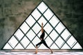 Young beautiful woman doing yoga asana Warrior I Pose on large triangular window background