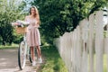 young beautiful woman in dress with retro bicycle with wicker basket full of flowers