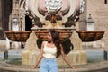 Young beautiful woman dressed in casual clothes sitting on the edge of a marble fountain in front of the cathedral of seville. The