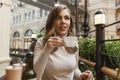 Young beautiful woman is drinking coffee in a cafe. Smiling blonde holding a white cup in her hands. Business meetings and rest Royalty Free Stock Photo