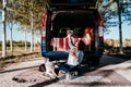 young beautiful woman drinking coffee or tea camping outdoors with a van and her two dogs. Travel concept