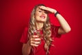 Young beautiful woman drinking a glass of water over red isolated background stressed with hand on head, shocked with shame and Royalty Free Stock Photo