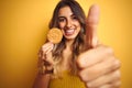 Young beautiful woman eating biscuit over grey isolated background happy with big smile doing ok sign, thumb up with fingers, Royalty Free Stock Photo