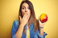 Young beautiful woman eating fresh healthy mango over yellow background cover mouth with hand shocked with shame for mistake, Royalty Free Stock Photo