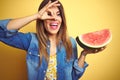 Young beautiful woman eating fresh healthy watermelon slice over yellow background with happy face smiling doing ok sign with hand Royalty Free Stock Photo