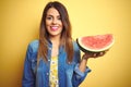 Young beautiful woman eating fresh healthy watermelon slice over yellow background with a happy face standing and smiling with a Royalty Free Stock Photo