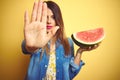 Young beautiful woman eating fresh healthy watermelon slice over yellow background with open hand doing stop sign with serious and Royalty Free Stock Photo